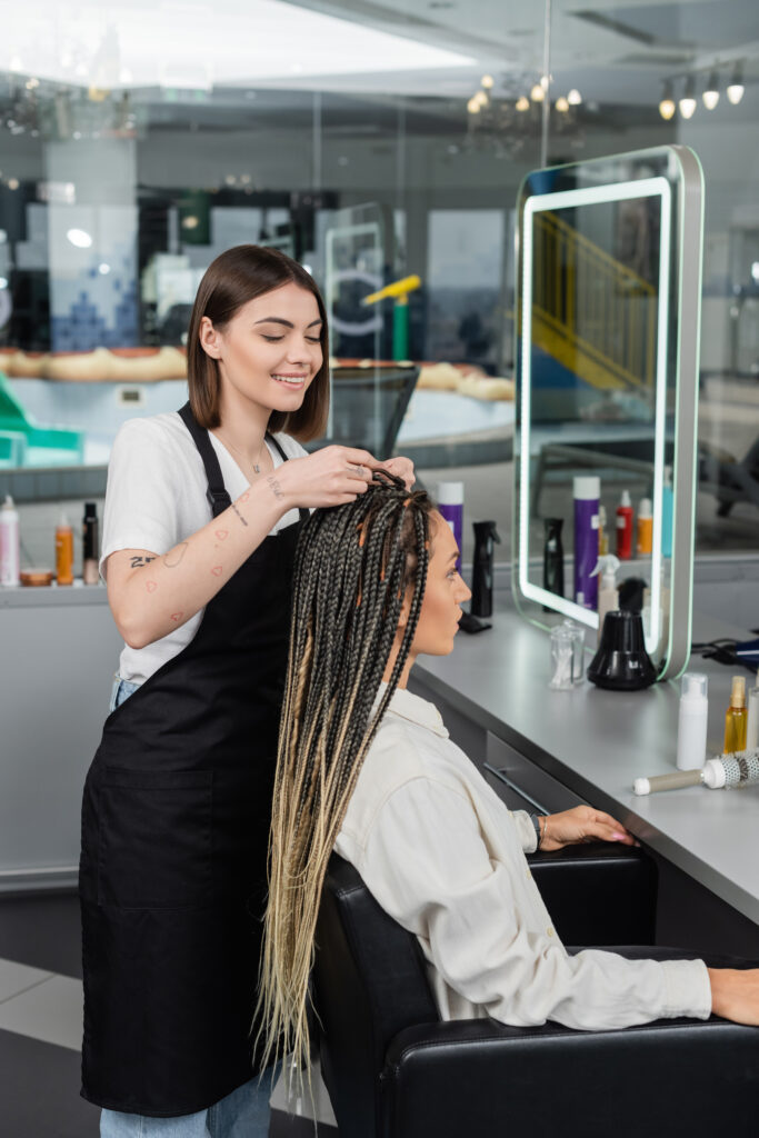 Happy hairdresser braiding hair of a woman in the salon.